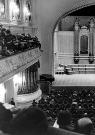 Portada:Plano general de Arthur Rubinstein (perfil derecho) sentado al piano en el escenario. Fotografía tomada desde el fondo de la sala