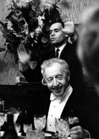 Portada:Plano general de un hombre, de pie, detrás de Arthur Rubinstein sentado a la mesa