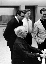 Portada:Plano medio de Arthur Rubinstein sentado al piano rodeado de un hombre, John Rubinstein, Max G. Willcox (Productor) y Aniela Rubinstein, todos charlando