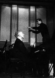 Portada:Plano medio de Arthur Rubinstein (perfil derecho) sentado al piano, al fondo el director de la orquesta con la batuta en la mano derecha, dirigiendo