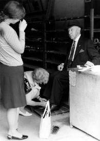 Portada:Plano general de Aniela Rubinstein de cuclillas atando los cordones del zapato a Arthur Rubinstein que está sentado mientras Alina Rubinstein les observa