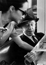 Portada:Plano medio de Arthur Rubinstein ojeando un periódico en japonés junto a una traductora