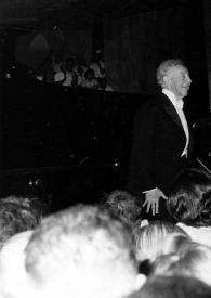 Portada:Plano medio de Arthur Rubinstein (perfil derecho) de pie, saludando al público (delante de él) con la orquesta al fondo
