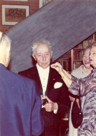 Portada:Plano medio de Arthur Rubinstein con una copa en la mano posando mientras Aniela Rubinstein habla con él. Detrás una mujer sonriendo