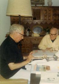 Portada:Plano medio de Arthur Rubinstein (perfil derecho) sentado en una mesa con Sol Hurok mirando unos papeles