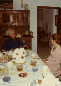 Portada:Plano general de la mesa, sentados: Arthur Rubinstein y una mujer (perfil izquierdo) charlando