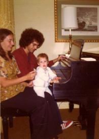 Portada:Plano general de Judith West (perfil derecho), John Rubinstein (perfil derecho) y Jessica Rubinstein (de frente) sentados al piano, Jessica sobre las rodillas de Judy tocando el piano