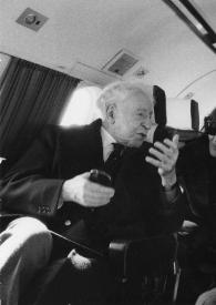 Portada:Plano medio de Arthur Rubinstein sentado en un asiento del avión, una mujer sentada en el asiento detrás de él y Herbert Kloiber sentado en un asiento al lado de Arthur Rubinstein charlando los tres.