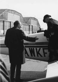 Portada:Plano general de un hombre ayudando a Arthur Rubinstein a bajar de la avioneta, detrás, el piloto