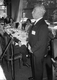 Portada:Plano general de Arthur Rubinstein (perfil izquierdo), de pie, hablando por un micrófono a otros invitados