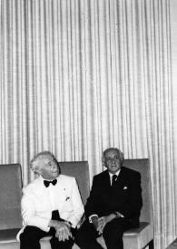 Portada:Plano general de Arthur Rubinstein y Moshe Kol sentados en unos sillones observando a un hombre hablar de pie a través de un micrófono