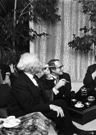 Portada:Plano general de Arthur Rubinstein sentado en un sofá y fumando un puro, un hombre y Jacques Chancel sentados en el suelo, una mujer sentada en un sillón y Thierry Leluron disponiéndose a sacarles una fotografía