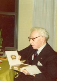 Portada:Plano medio de Arthur Rubinstein (medio plano izquierdo) sentado en una silla abriendo una caja de puros
