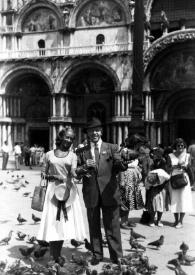 Portada:Plano general de Eva y Arthur Rubinstein posando en la Plaza de San Marco mientras dan de comer a las palomas