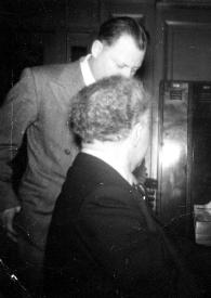 Portada:Plano medio de Fredric Rand Mann charlando con Arthur Rubinstein que está sentado al piano y charlando también con un hombre
