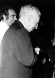 Portada:Plano medio de Arthur Rubinstein charlando con una mujer, detrás un hombre y una mujer charlando