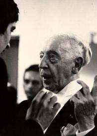 Portada:Plano medio de Arthur Rubinstein (medio perfil izquierdo) con la mano izquierda levantada y charlando con un hombre