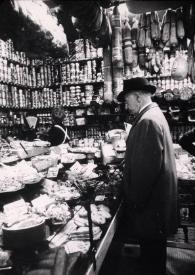 Portada:Plano general de Arthur Rubinstein (perfil izquierdo) observando el género de una tienda de alimentos, al fondo una vendedora de espaldas.