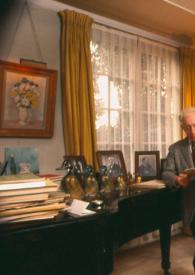Portada:Plano general de Arthur Rubinstein de pie apoyado en el piano, con chaqueta de pata de gallo y con un puro en la mano, mientras lee un libro