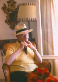 Portada:Plano medio de Arthur Rubinstein sentado con sombrero encendiendo un puro